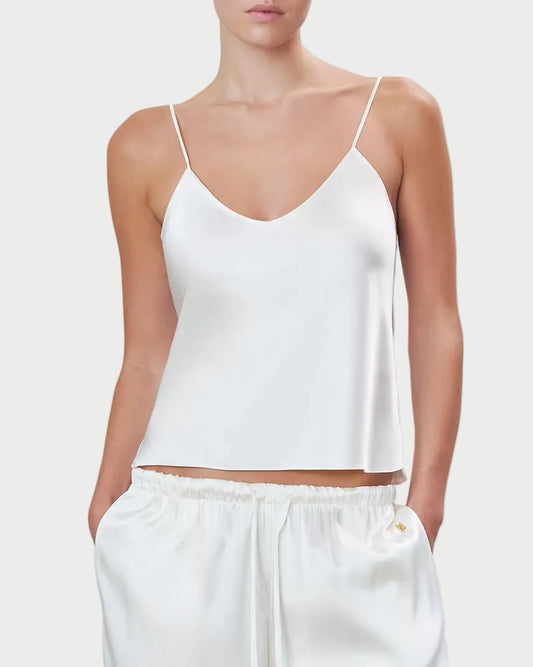 Woman wearing a white spaghetti strap top and pants on a light gray background