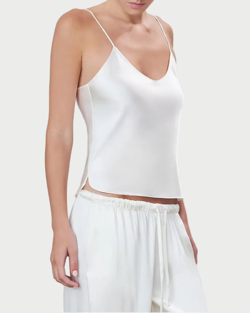 Woman wearing a white spaghetti strap top and white pants on a light gray background