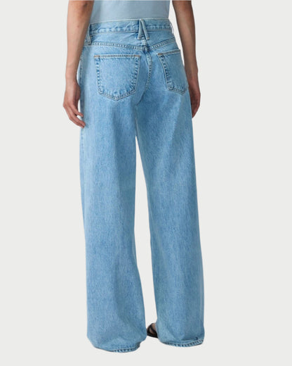 A person with long, dark hair stands against a plain white background wearing a light gray T-shirt and loose-fitting SLVRLAKE's Mica Jeans in Clear Skies. The relaxed silhouette exudes a vintage-inspired vibe, while the fabric tells stories of regenerative cotton.