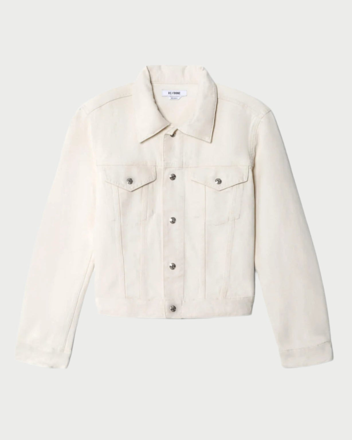 The RE/DONE Baby Trucker Jacket is an ivory, 70’s-inspired style with long sleeves, buttoned cuffs, a front button closure, and two chest pockets, shown on a plain white background.
