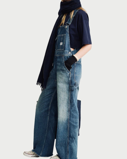 Person wearing denim overalls and a dark jacket on a white background