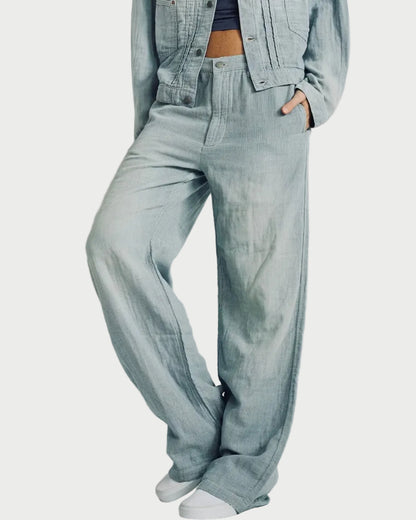 A person wearing light-wash wide-leg denim pants with a matching cropped denim jacket and white sneakers, standing against a plain light gray studio background.