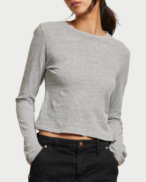 Woman wearing a gray long-sleeve top and black pants against a light background