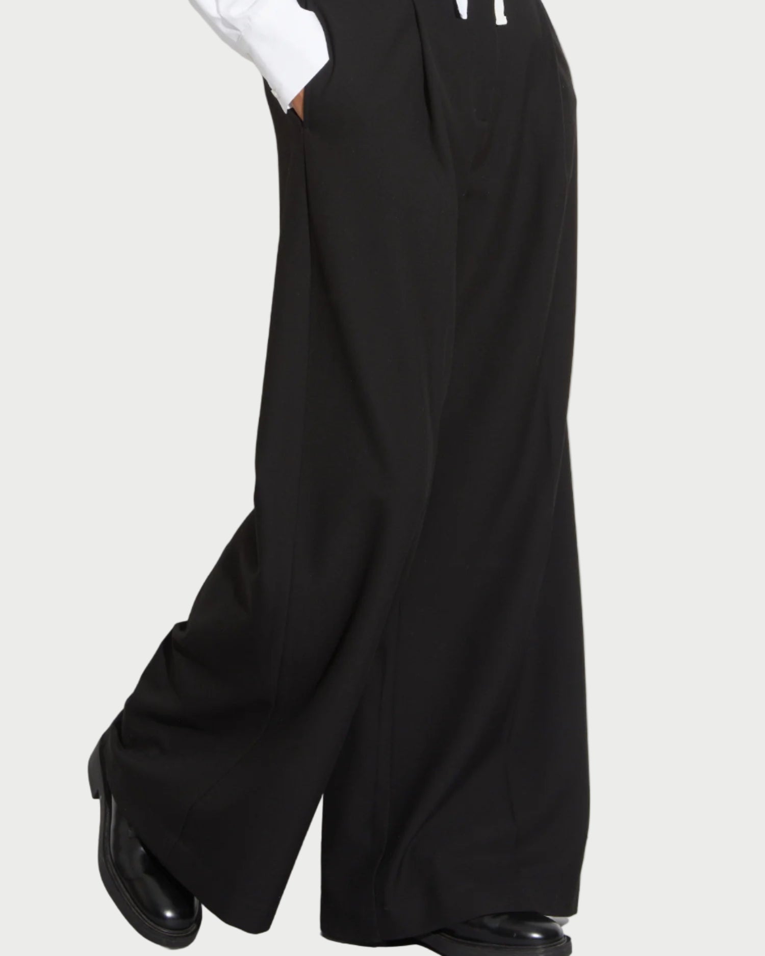 A person wearing Saint Art NY's Tiffany Wide Leg Pants and black shoes is captured mid-step, showing only their lower half against a plain background. The pants’ wrinkle-resistant fabric keeps the look sharp all day.