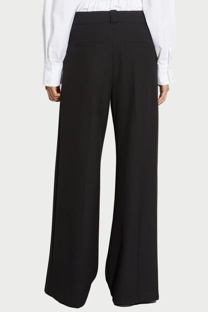 Someone wearing Saint Art NY’s Tiffany Wide Leg Pants in black and a white long-sleeve shirt, seen from the back against a plain background.