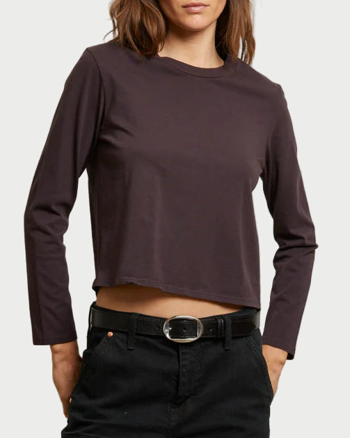Person wearing a long-sleeve brown top and black pants against a plain background