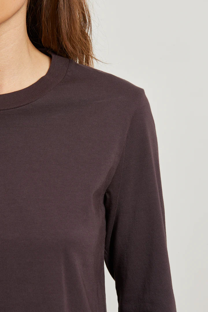 Close-up of a person wearing a dark brown long-sleeve shirt against a light gray background