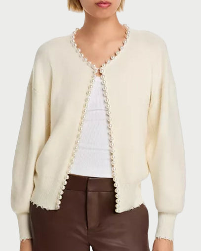 Woman wearing a cream cardigan with lace trim over a white top and brown pants on a white background