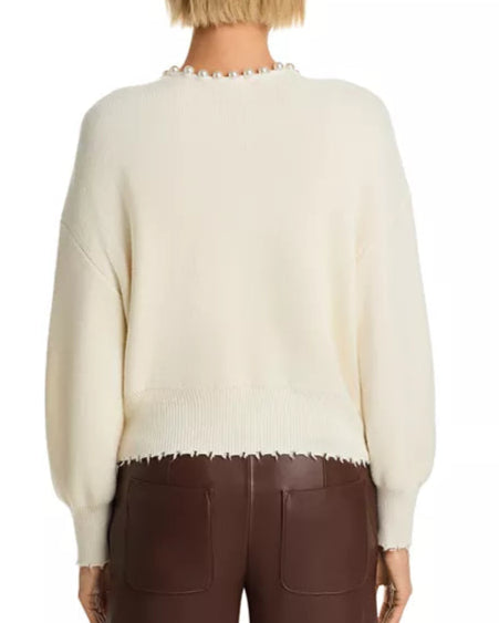 Person wearing a cream sweater with a subtle pattern and brown pants on a white background