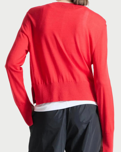 Person wearing a red sweater over a white shirt with black pants on a white background