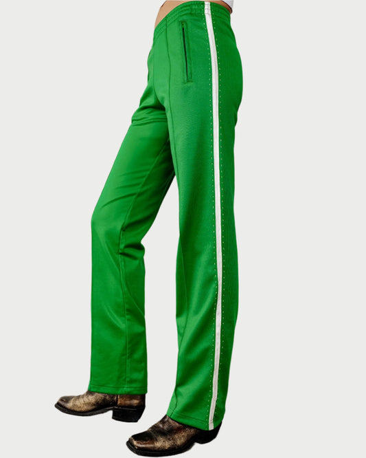 A person wearing RE/DONE Sunland Track Pant in bright green with a white side stripe and black boots, shown from the waist down against a plain background.