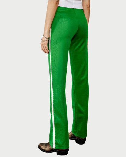 A person wearing RE/DONE Sunland Track Pant in bright green with a white side stripe, paired with a white top, bracelets, and black shoes, stands facing away from the camera against a plain background for a sporty Western-inspired look.