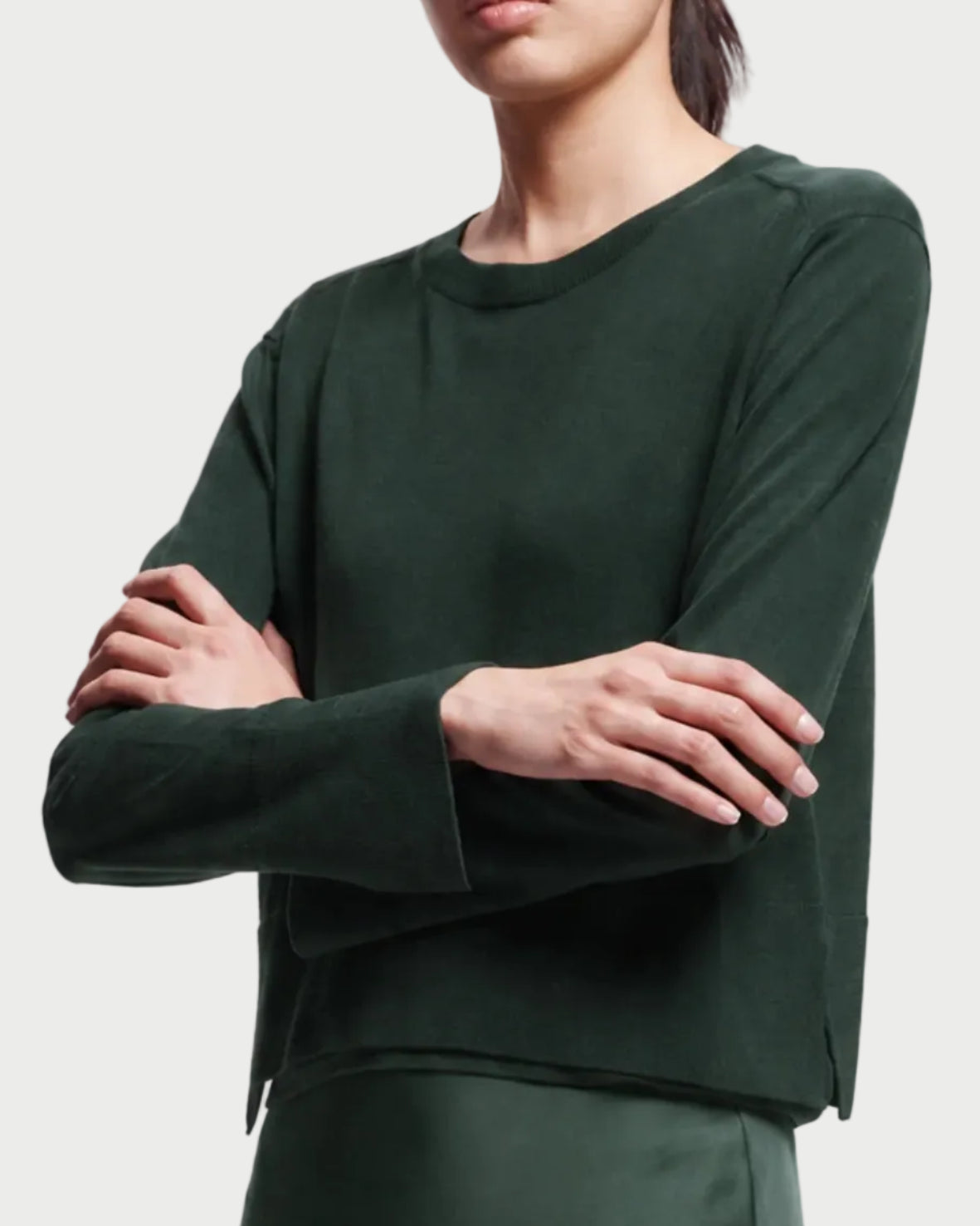 A person wearing a Saint Art Elodie Sweater in forest green merino wool with a crew neckline and slightly flared cuffs.