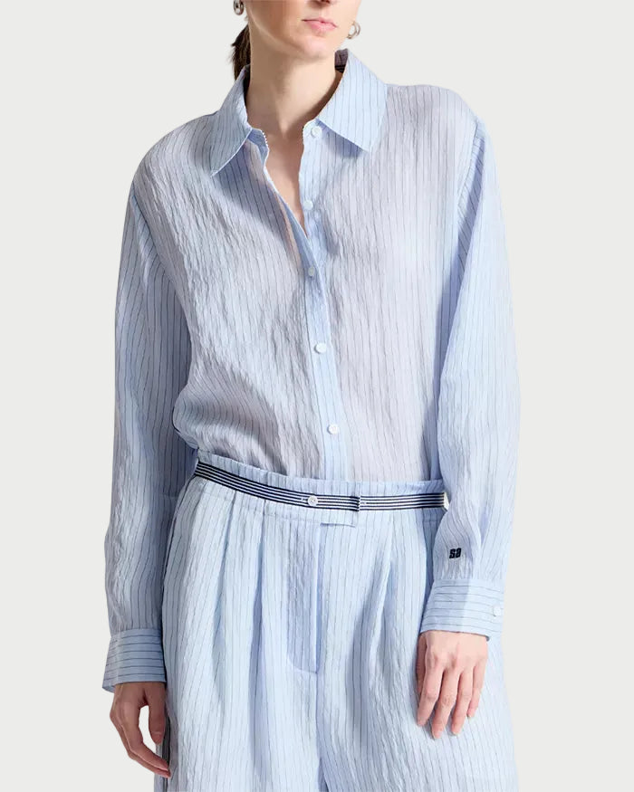 Woman wearing a light blue striped shirt and white pants with a belt on a white background