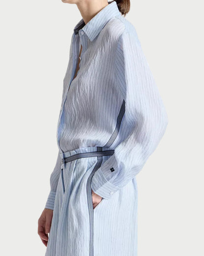 Person wearing a light blue striped dress with a belt on a white background