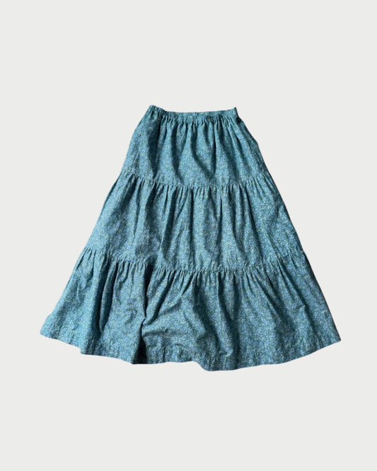 The 171 Liberty Print Skirt by A Friend Made is a pre-loved, blue midi skirt in a subtle floral Liberty print with a flowy tiered silhouette, shown flat on a white background. Available exclusively at WEST.