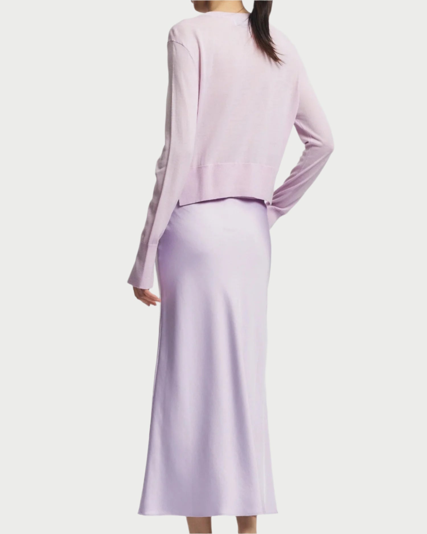 A person with long hair is shown from the back in a Saint Art NY Nixon Cropped Cardigan paired with a matching ankle-length skirt. The luxury knitwear ensemble features a soft, flowing texture against a plain white background.