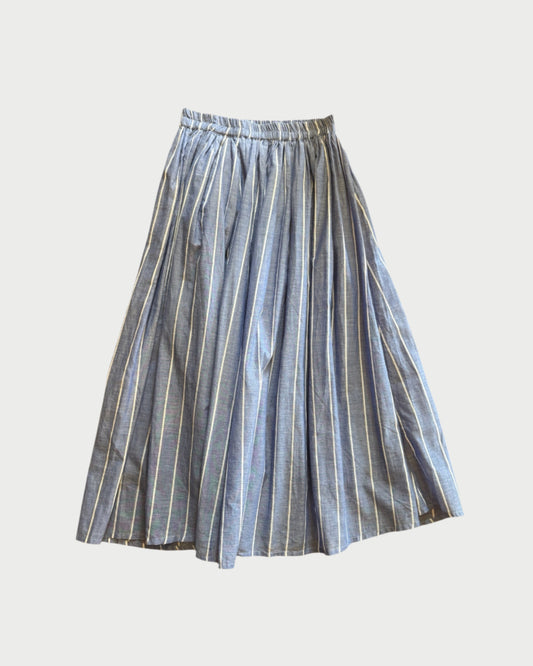 The 178 Hab Stripe Skirt by A Friend Made is a blue and white vertical striped, pleated midi skirt with an elastic waistband, shown laid flat on a white background.