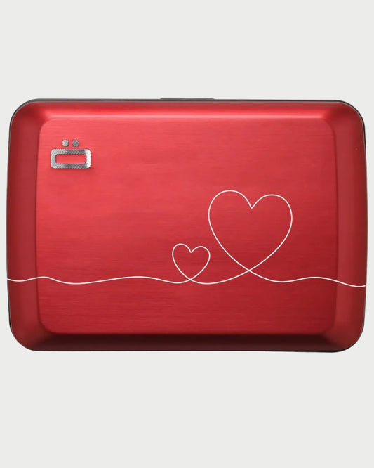 The OGON Design Oslo Aluminum Card Holder is a red, rectangular case with a metallic finish, two interlocking white heart outlines, RFID protection, and a small OGON Design logo in the top left corner.