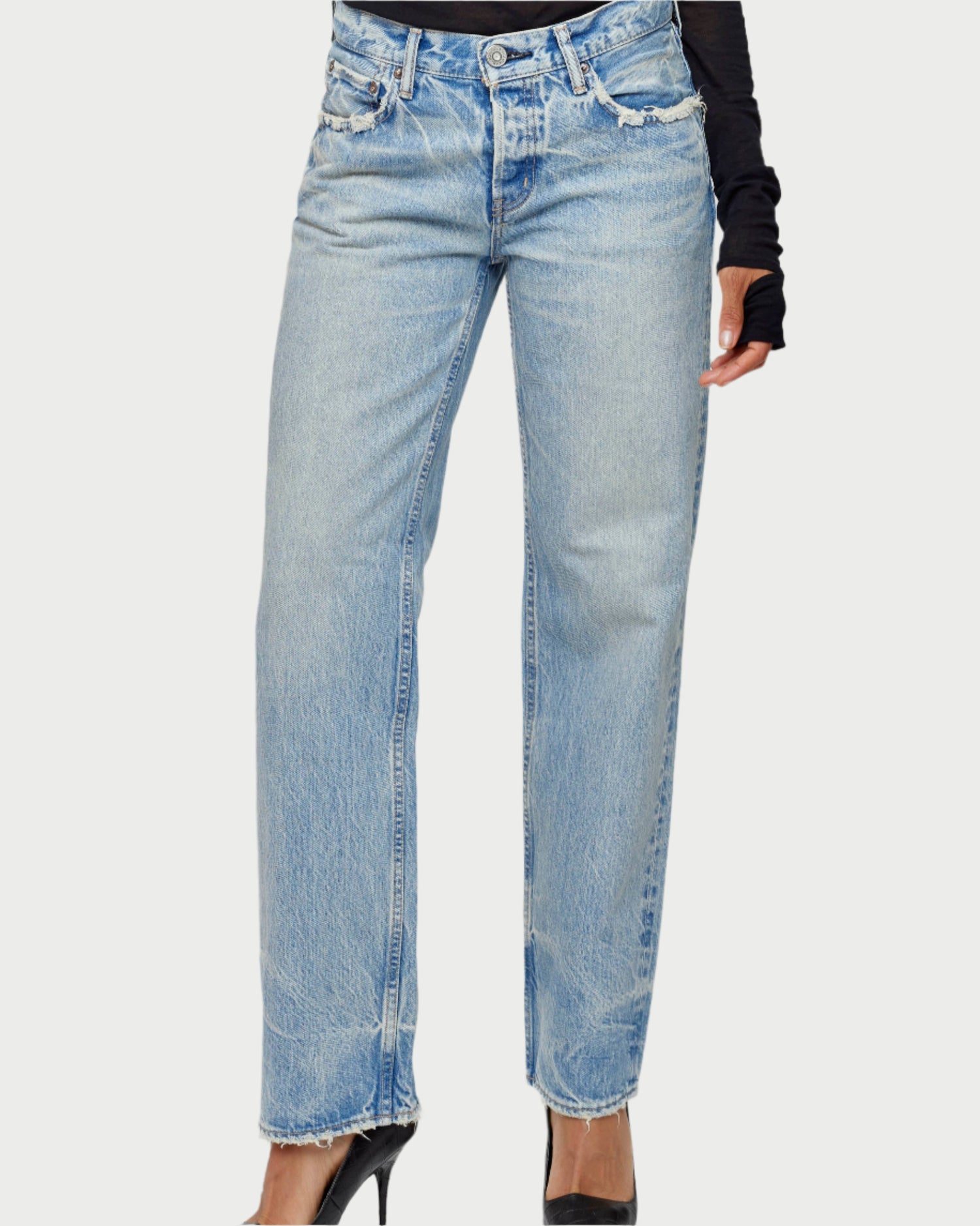 A person is styled in Moussy's Wildwood Straight Leg Jeans in light blue, showcasing distressed details and frayed hems. These high-waisted jeans complement a black long-sleeve top and black pointed heels against a light gray backdrop.