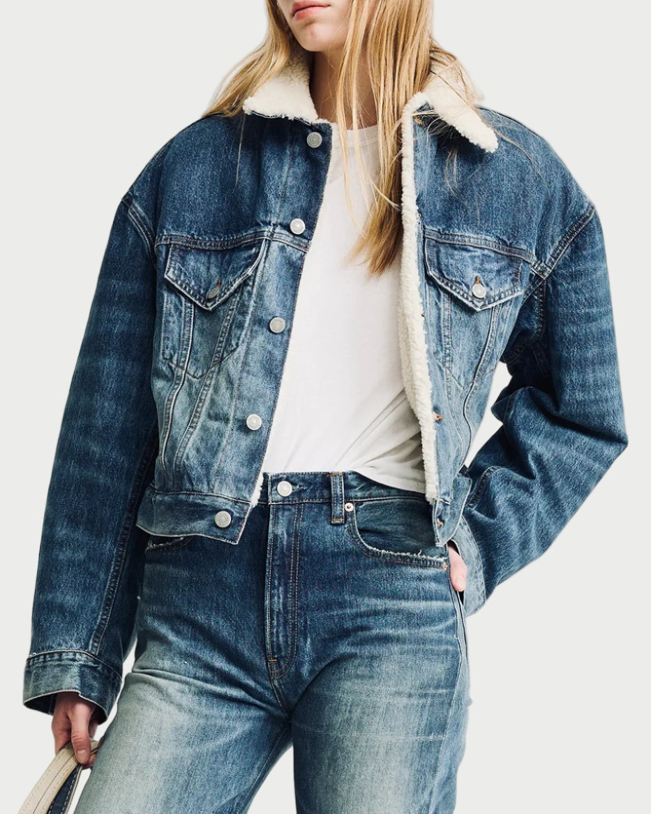 Person wearing a denim jacket and jeans holding a white tote bag on a light gray background