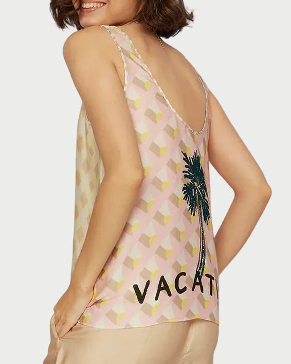 Woman wearing a sleeveless top with palm tree design and 'Vacay' text, standing against a clear blue sky.