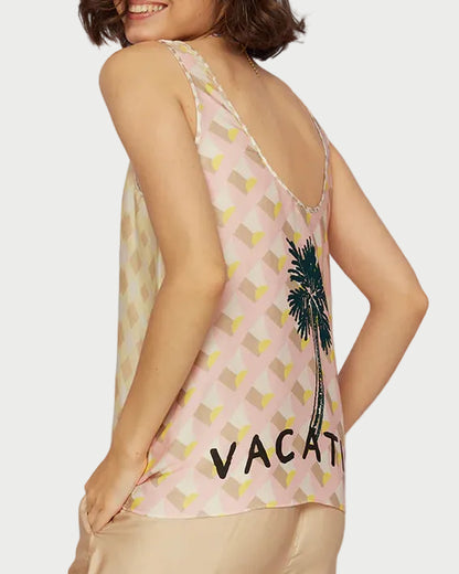 Woman wearing a sleeveless top with palm tree design and 'Vacay' text, standing against a clear blue sky.