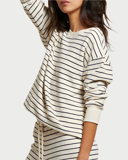 A woman wears the cream-colored, relaxed fit perfectwhitetee Tyler Terry Pullover and matching striped pants. Her right arm is raised, and her face is partially turned away from the camera.