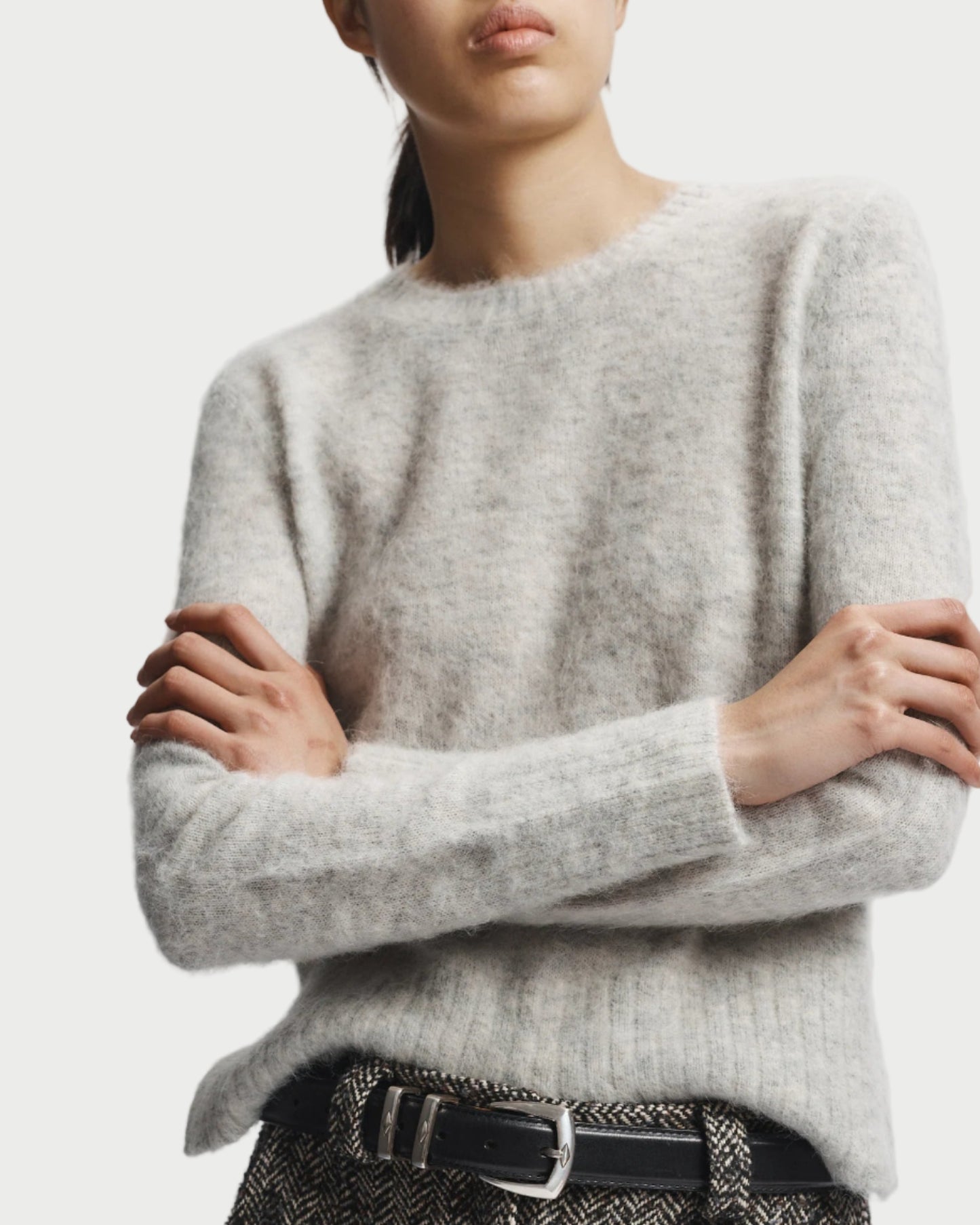 Person wearing a light gray sweater and patterned pants with a white background