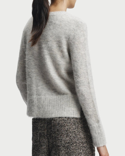 Person wearing a light gray sweater and patterned pants on a white background