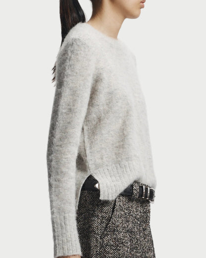 Person wearing a light gray sweater and patterned pants on a white background