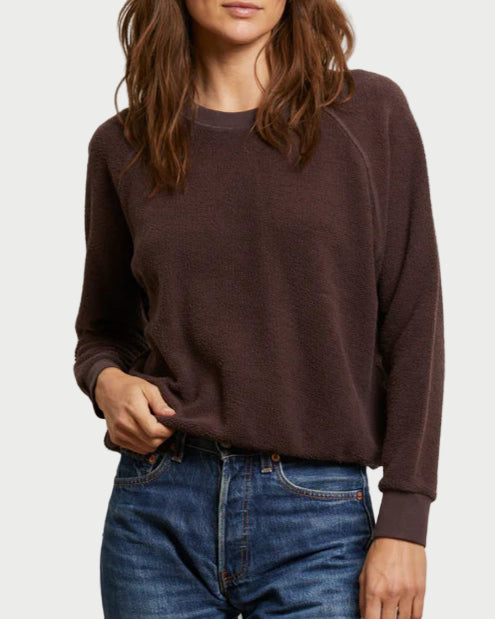 Woman wearing a brown sweater and blue jeans against a plain background