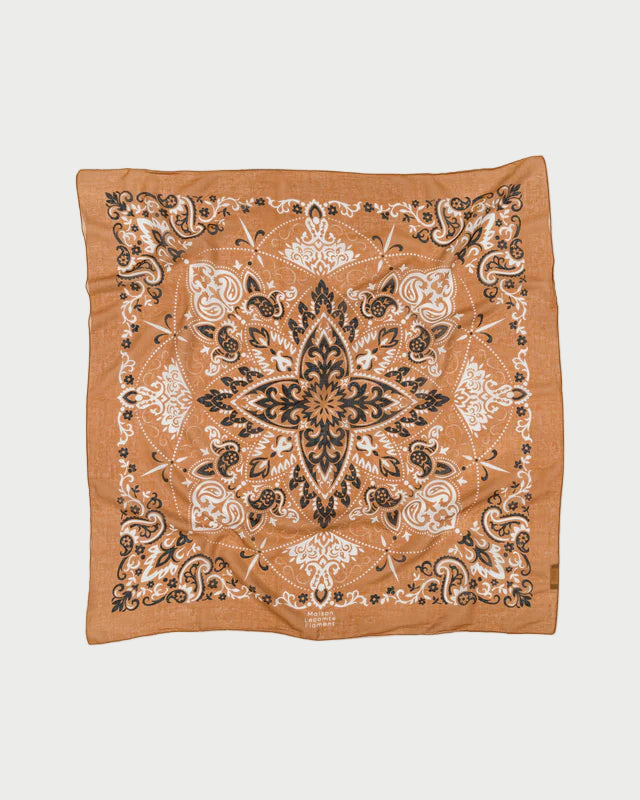 The Bandana Scarf Camel by Maison Lecomte Flament is a square, tan cotton voile bandana featuring an intricate black and white paisley pattern with a large symmetrical floral design at the center.