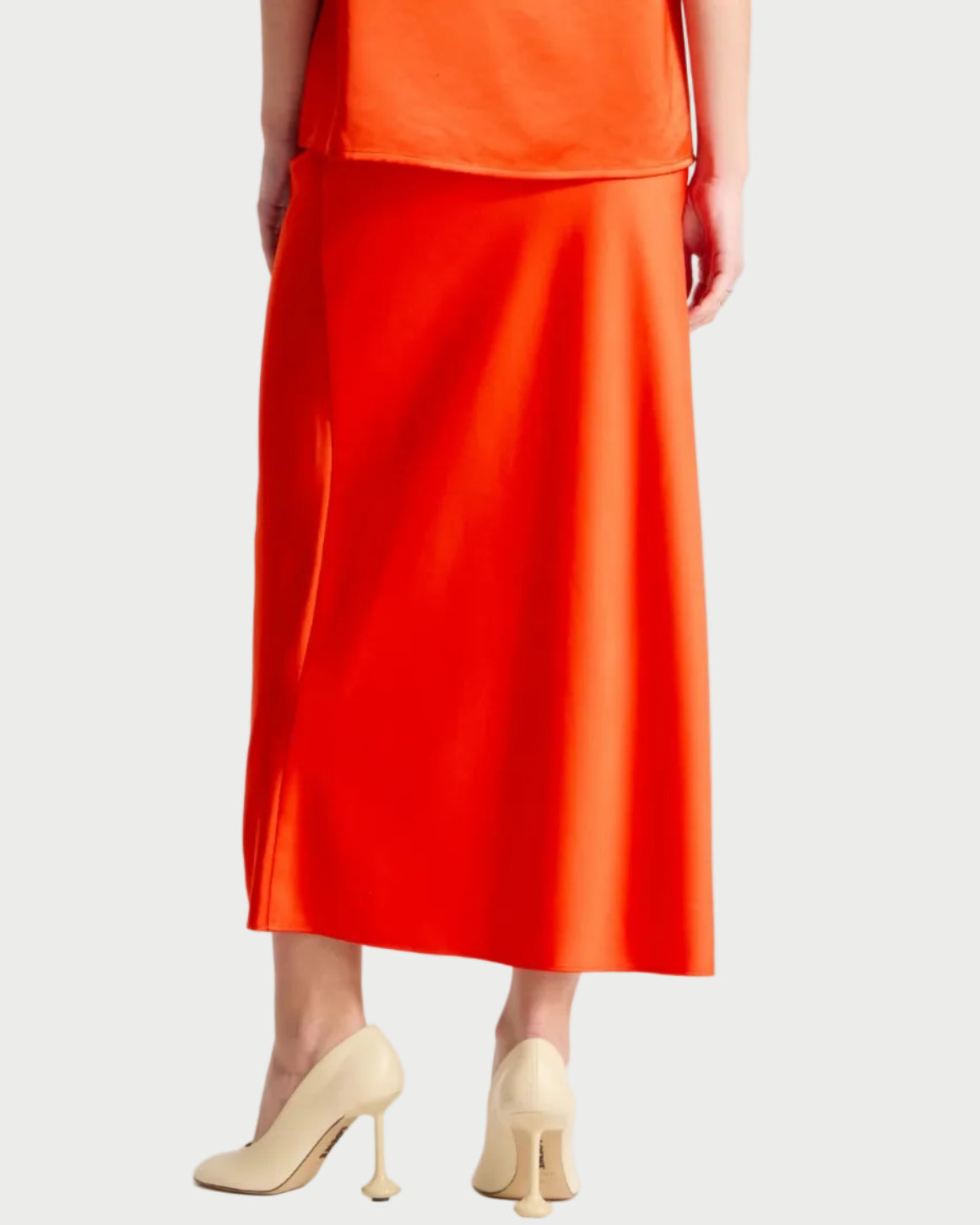 Person wearing a bright orange sleeveless top and skirt set on a white background