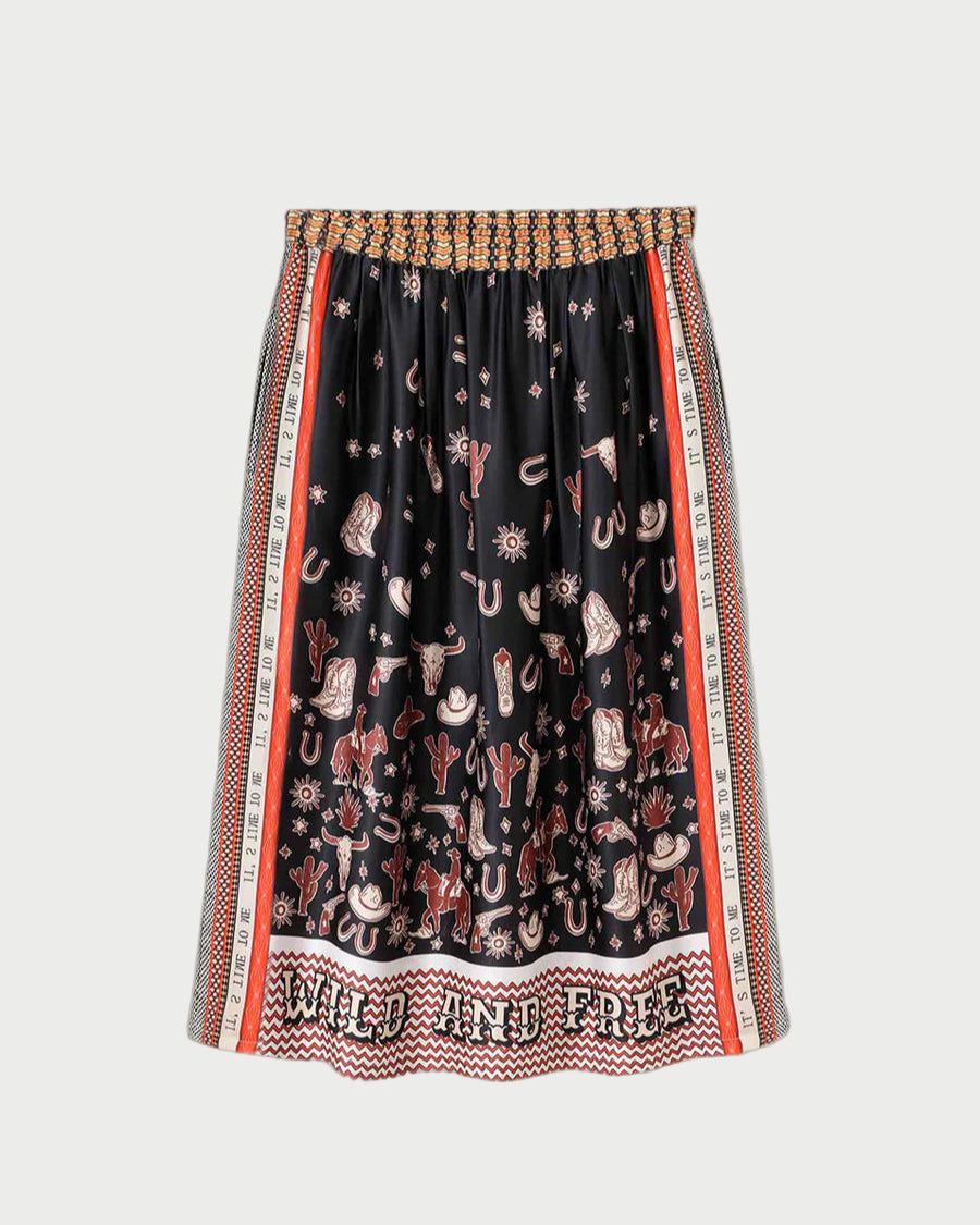 The ME369 Vanessa Skirt Rodeo is a black pleated midi skirt with a vibrant Western rodeo print—cowboy hats, boots, cacti, and horses. “WILD AND FREE” accents the hem, and the elastic waistband features a woven design.