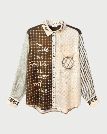 A long-sleeve button-up shirt with a patchwork design featuring brown gingham, cream mesh, black-and-white stripes, and graphic prints, displayed flat against a white background.