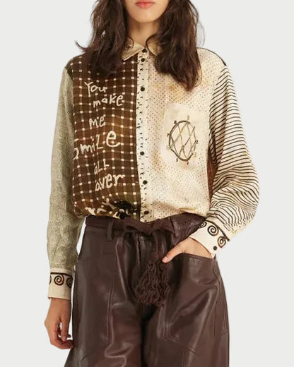 A model is shown from the head to the feet wearing a long-sleeve button-up shirt with a brown and beige patterned yoke and striped sleeves, paired with wide-leg brown faux-leather trousers and black pointed boots, against a plain white studio background.