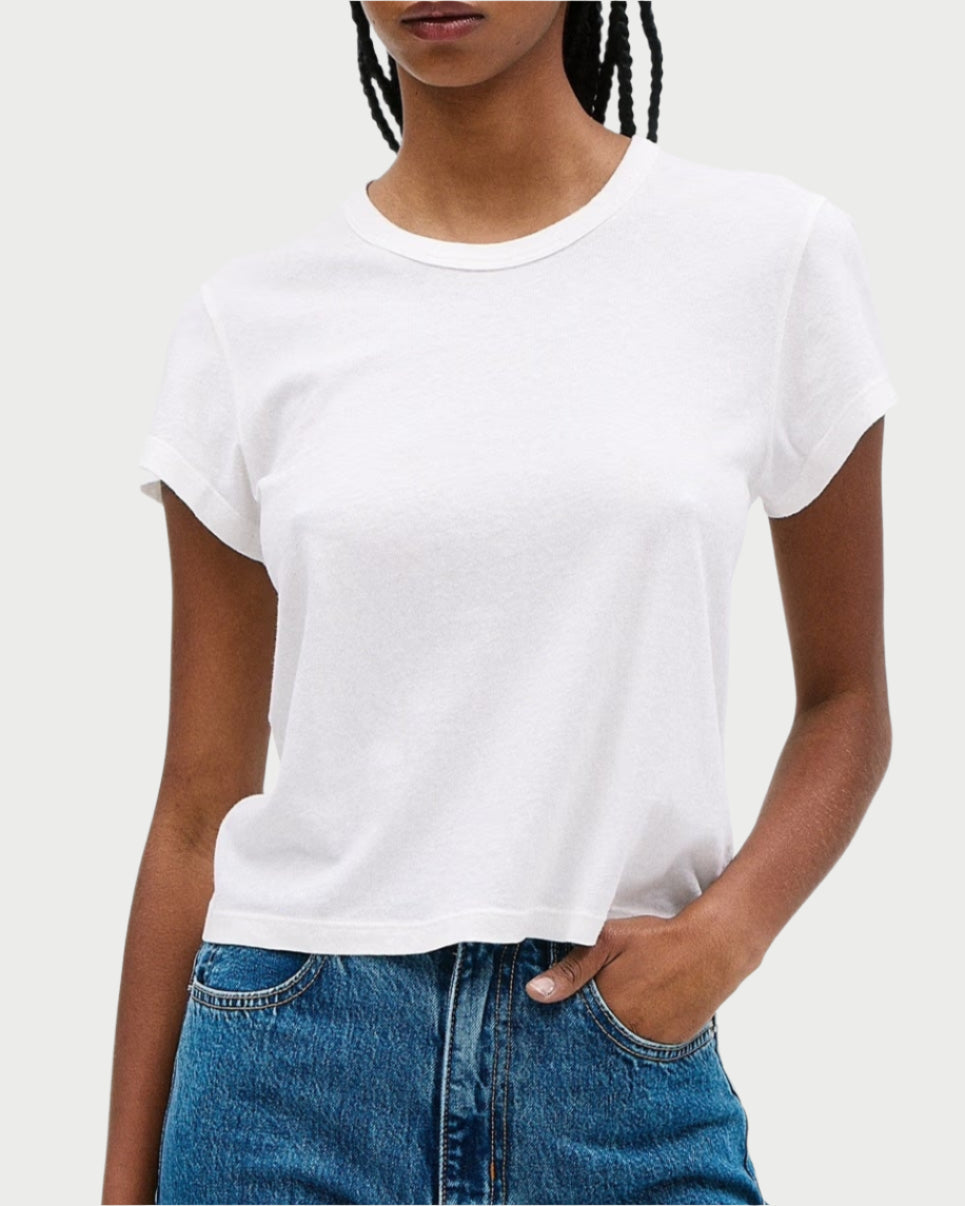 A person, wearing an SLVRLAKE Easy Lightweight Tee—a plain white T-shirt with a relaxed fit and short sleeves—and SLVRLAKE blue jeans, stands with one hand in their pocket against a light gray background.