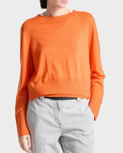 Person wearing an orange sweater and gray pants on a white background