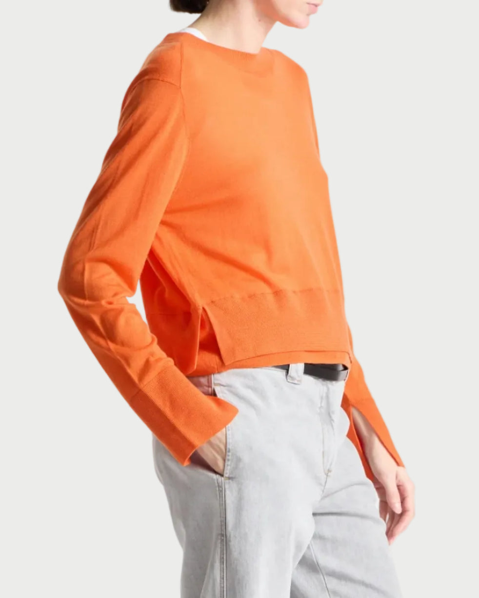 Person wearing an orange top and light gray pants on a white background