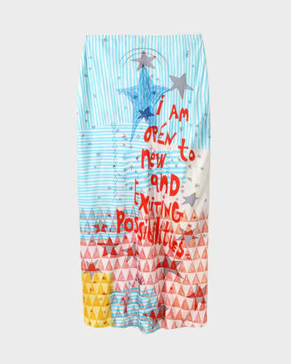 The ME369 Blakely Slip Skirt by ME369 features vibrant geometric patchwork—blue stripes, red and yellow triangles, and stars—with “i am open to new and exciting possibilities” in bold red text.