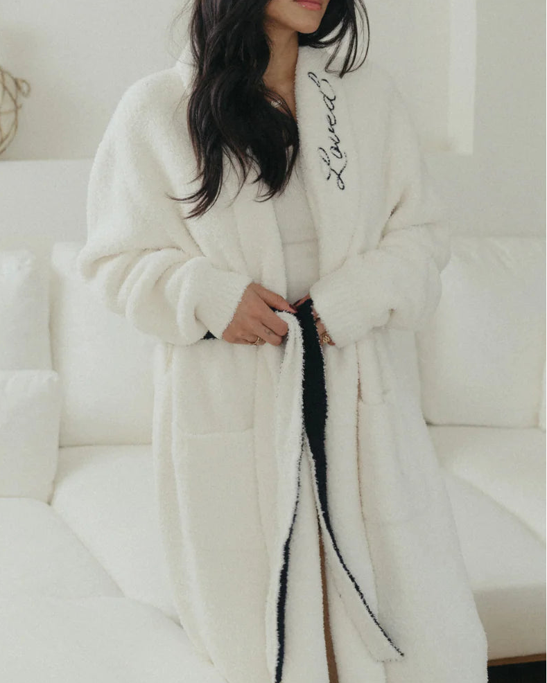 Woman wearing a white robe with black text sitting on a white couch.