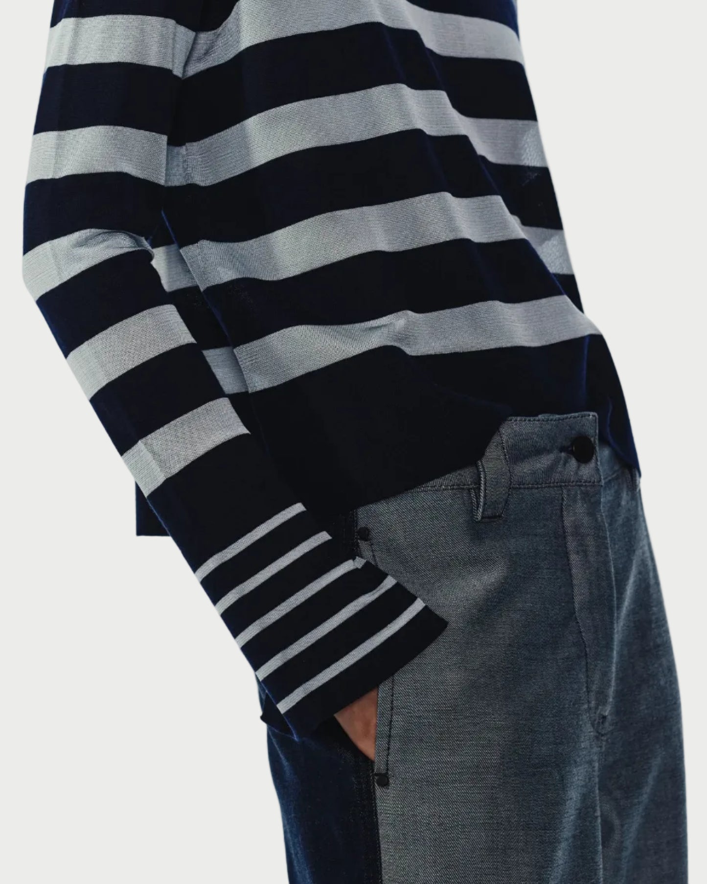 Person wearing navy and sky striped sweater and dark jeans on a light gray background