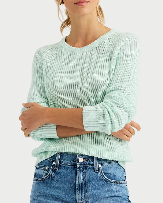 Woman wearing a light green sweater and blue jeans on a plain background