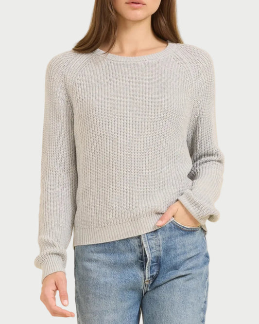 Woman wearing a gray sweater and blue jeans against a beige background