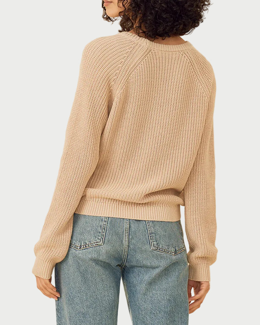 Woman wearing a beige sweater and blue jeans on a beige background