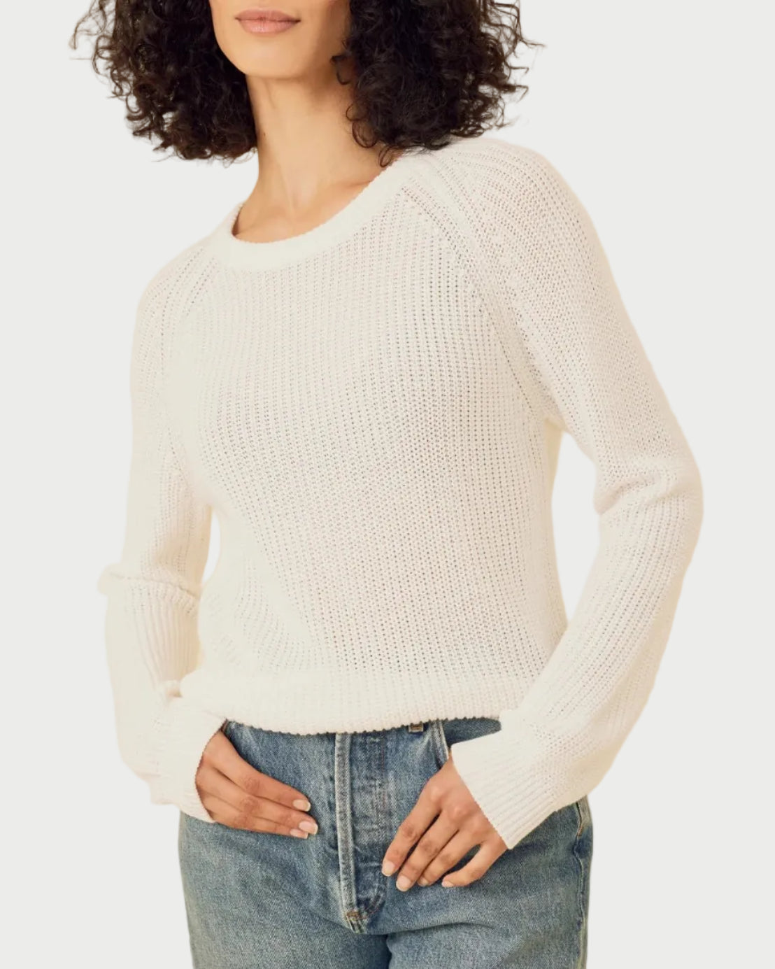 Woman wearing a white sweater and blue jeans against a beige background
