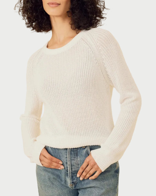 Woman wearing a white sweater and blue jeans against a beige background