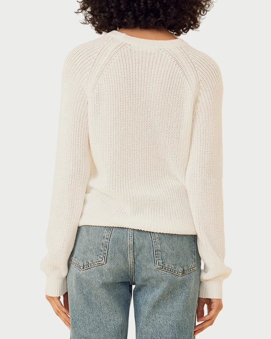 Person wearing a white sweater and blue jeans against a beige background