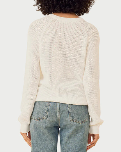 Person wearing a white sweater and blue jeans against a beige background